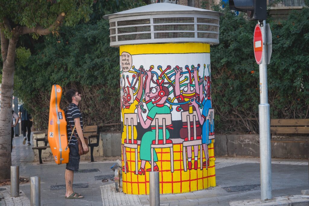 פיר בזק עגול מצויר בציור קיר צבעוני וצפוף בגווני צהוב ואדום, ברחוב בתל אביב
