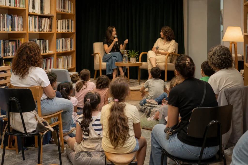 ילדים והורים יושבים במפגש ספרייה מול שתי דוברות על במה קטנה