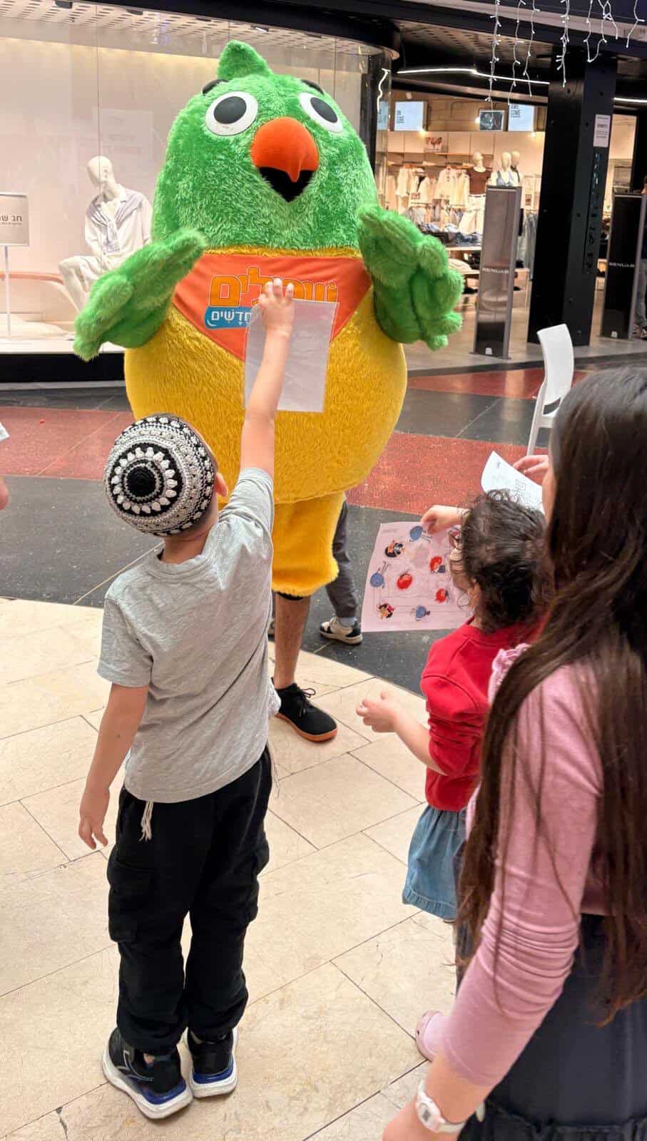 ילדים עומדים מול דמות ירוקה גדולה במרכז קניות