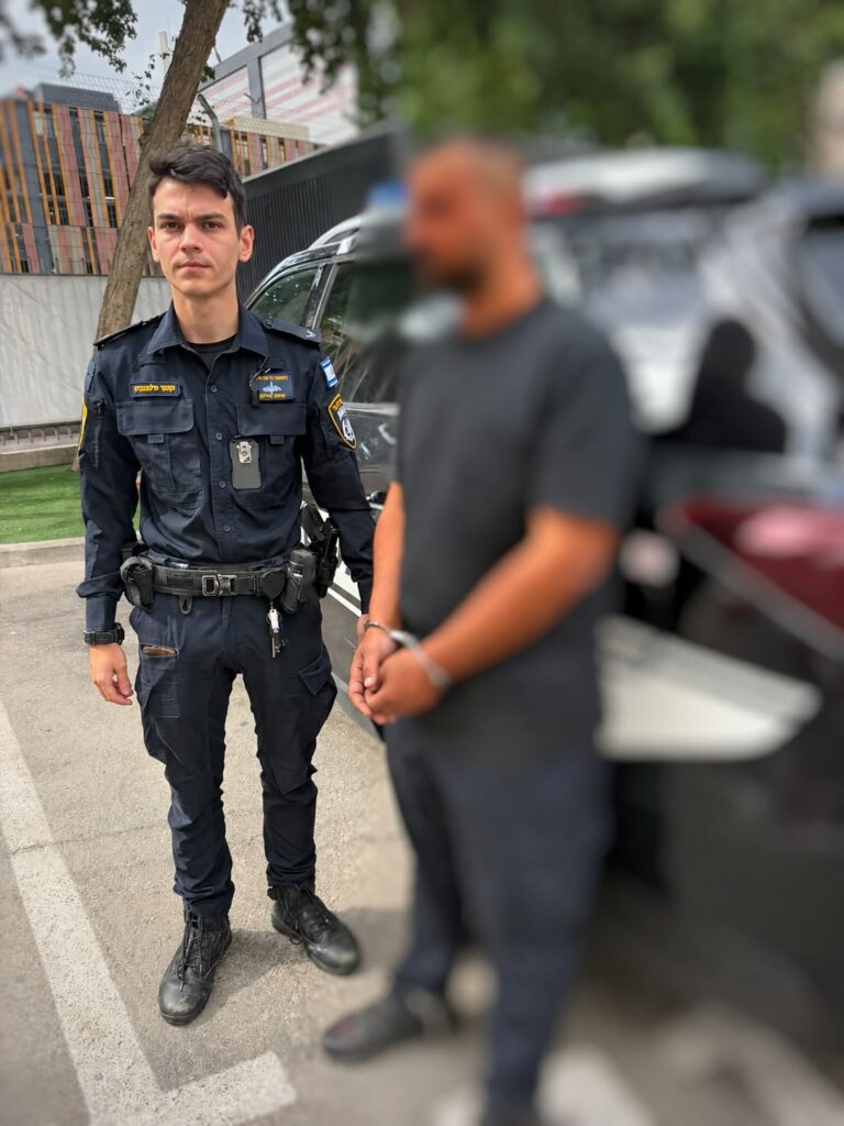 An officer beside a handcuffed suspect whose face is blurred after an arrest in Bat Yam